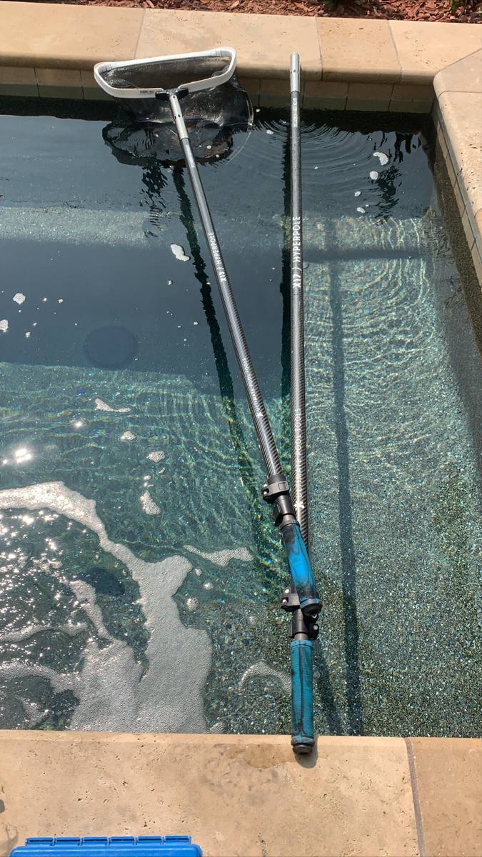 Pool pole and brush in clear water during weekly service